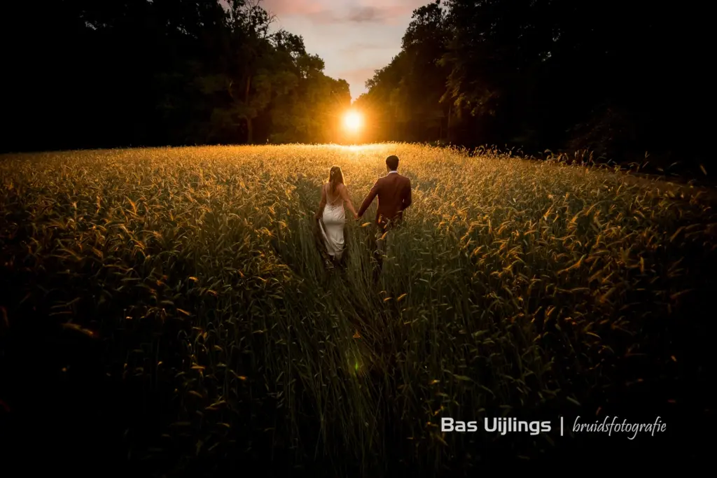 een bruid en een bruidegom die samen door een bloemenveld heen lopen hand in hand