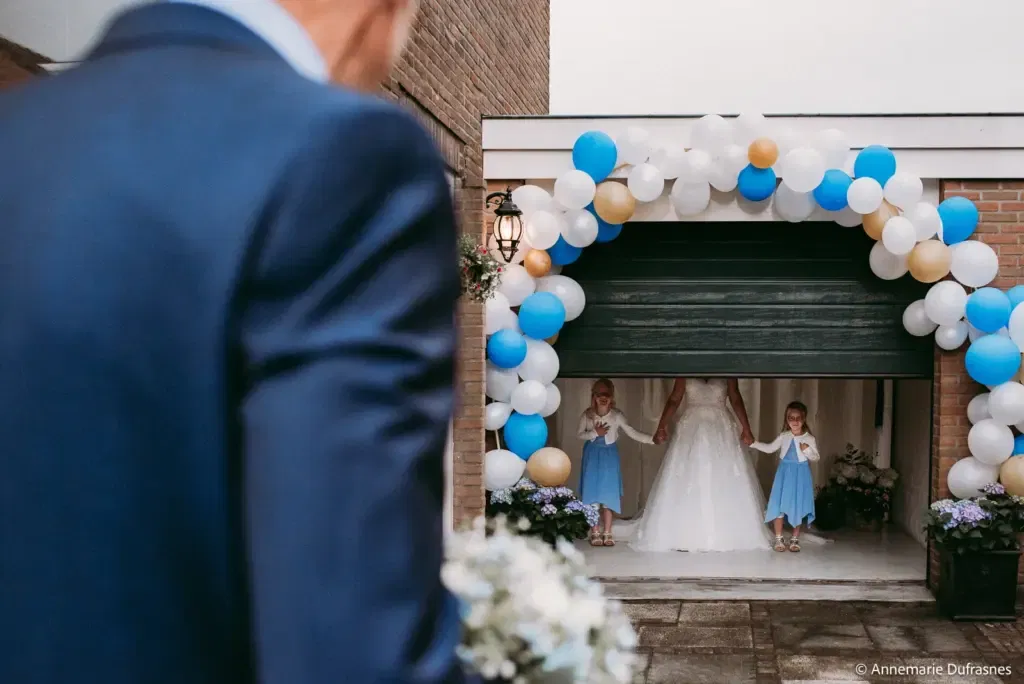 bruid en 2 bruidskinderen staan hand in hand in een garage die open gaat