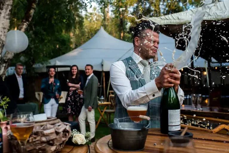 een man die een fles champagne openmaakt en er spuit allemaal champagne uit