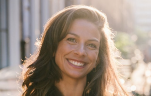 Sharon Schouten met een stralende glimlach poseert in natuurlijk zonlicht op een stadsstraat.