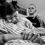 Kapper verzorgt het haar van een zittende vrouw tijdens een kwetsbaar moment, vastgelegd door Isabelle Hattink voor haar project De Straatkapper.